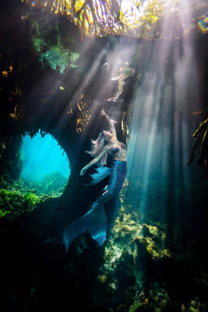 Real-life mermaid swimming through sunbeams in an ancient cenote