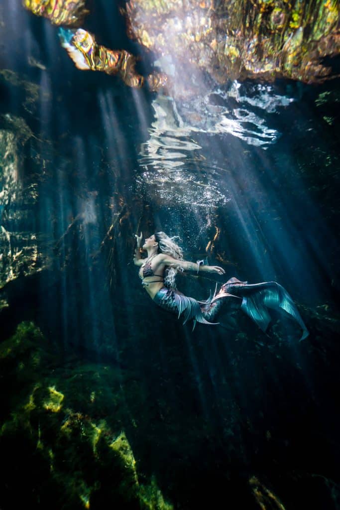 Professional mermaid gliding underwater through an ancient cenote