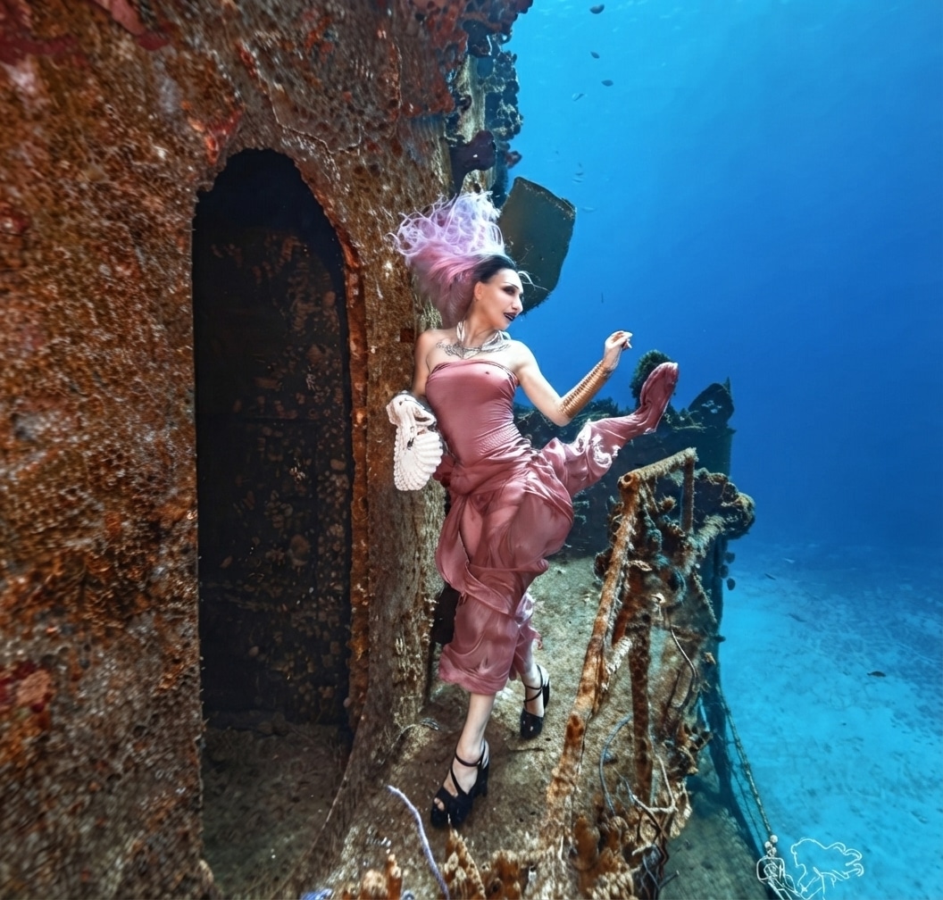 Underwater fashion model in a pink dress posing on a shipwreck