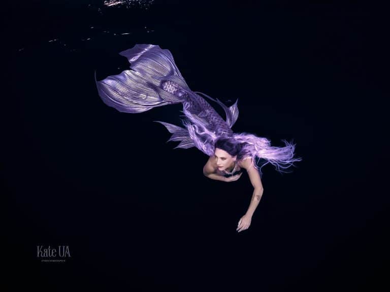 Real-life mermaid with a purple tail swimming through deep blue water
