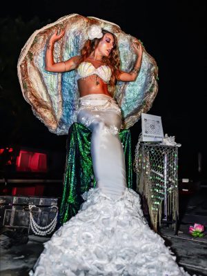 All-white mermaid posing in a clamshell throne at an elegant party